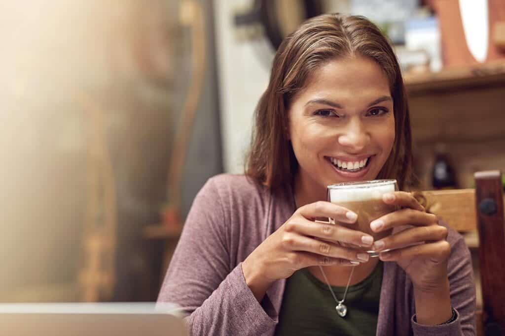 Woman drinking coffee and portrait in restaurant for happiness breakfast and beverage in morning Female person smile and positive with mug pride and comfort for weekend relax and peace in cafe